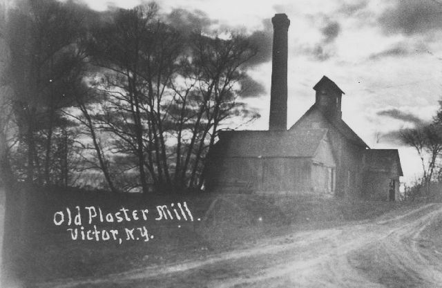 Wooden structure building of old plastermill on dirt road with smokestack